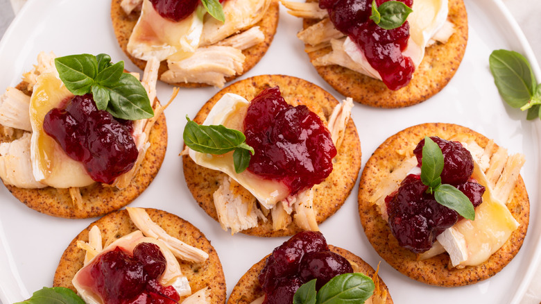 Close up of crackers with turkey, brie, cranberry sauce, and basil