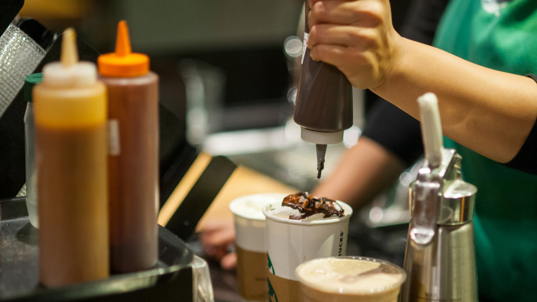 A Starbucks barista tops a drink with chocolate sauce from a squeeze bottle.