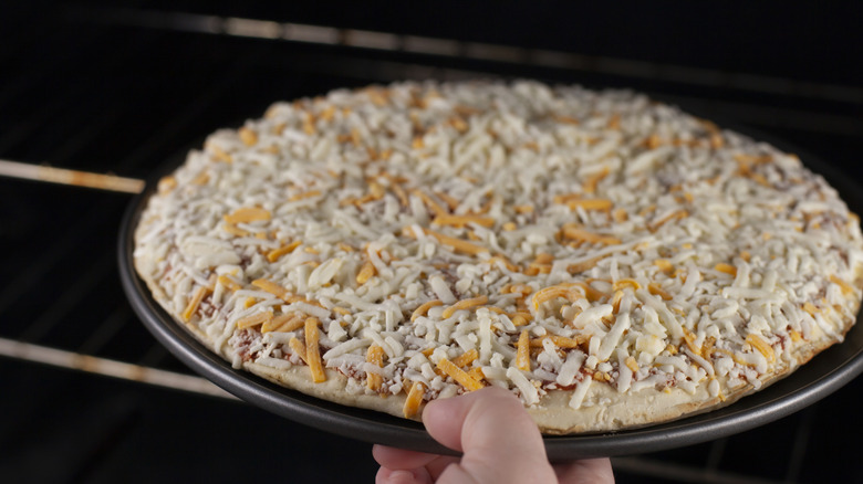 hand putting frozen pizza in oven