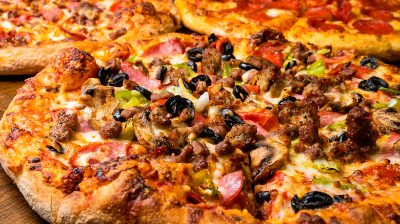 Supreme pizza with thick crust with a pepperoni and meat lovers pizza in the background