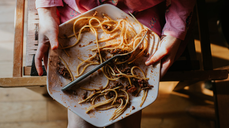 Someone holding a half-eaten plate of spaghetti.