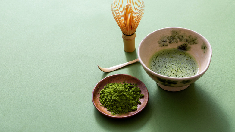 A bowl of perfectly made matcha, next to matcha powder.