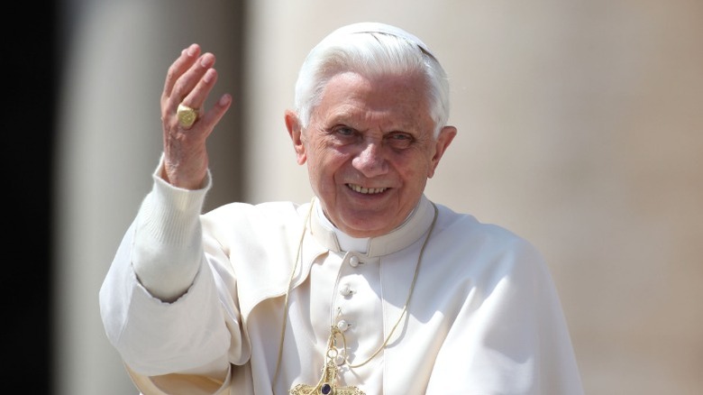 Pope Benedict XVI smiling and holding his hand up.