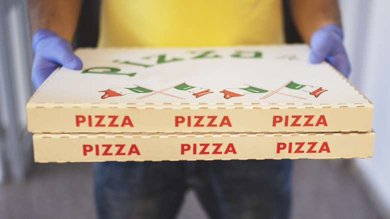 Person in yellow shirt holds two pizza boxes