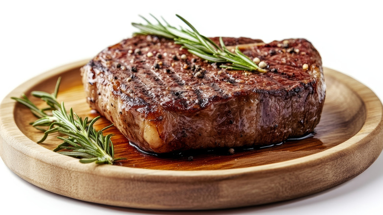 Grilled steak with rosemary and peppercorns on wood platter