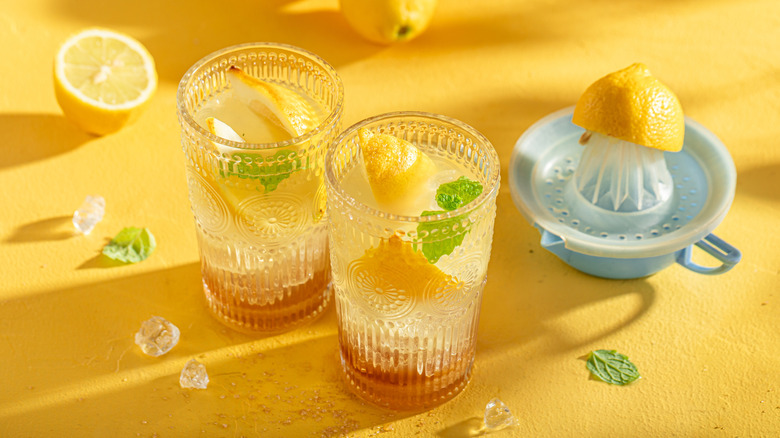 Glasses of lemonade alongside fresh lemons and juicer