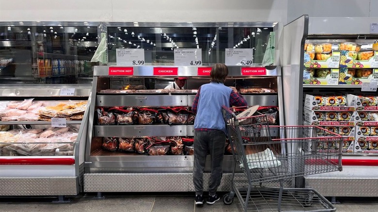 Costco customer browsing rotisserie chickens in store next to shopping cart