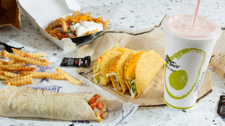 A Del Taco value meal, with tacos, burritos, fries, and a beverage on a white marble surface