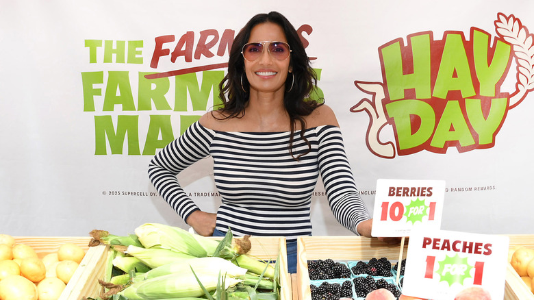 Padma Lakshmi standing at a farmers market fruit and vegetable stand