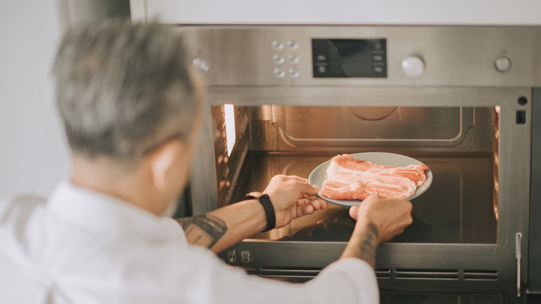 A man taking a plate of meat out of a microwave