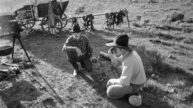 Black and white photo of cowboys sitting on the ground drinking from tin cups
