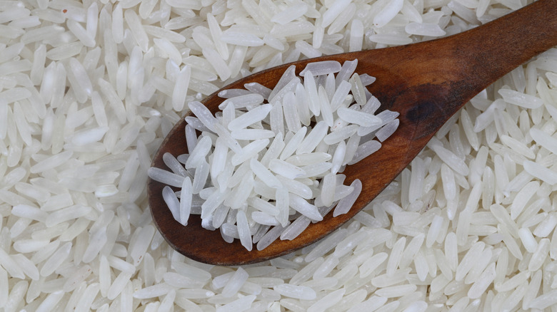 Uncooked rice grains in wooden spoon