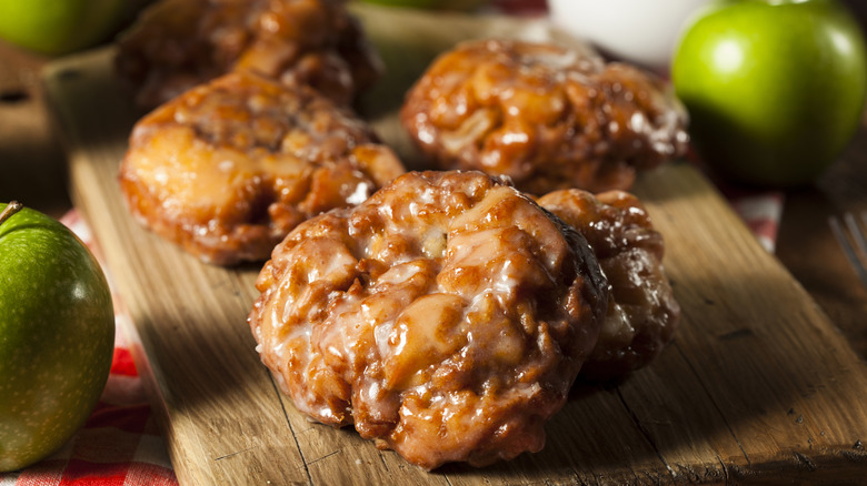 Apple fritters with glaze on wooden board with granny smith apples