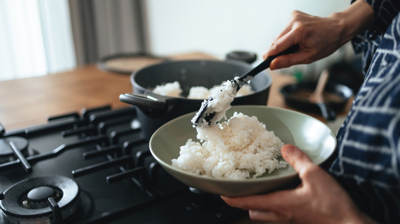 A hand scooping rice out of a pot.