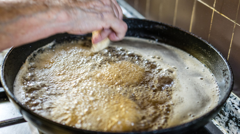 A home cook deep frying food in a shallow pan