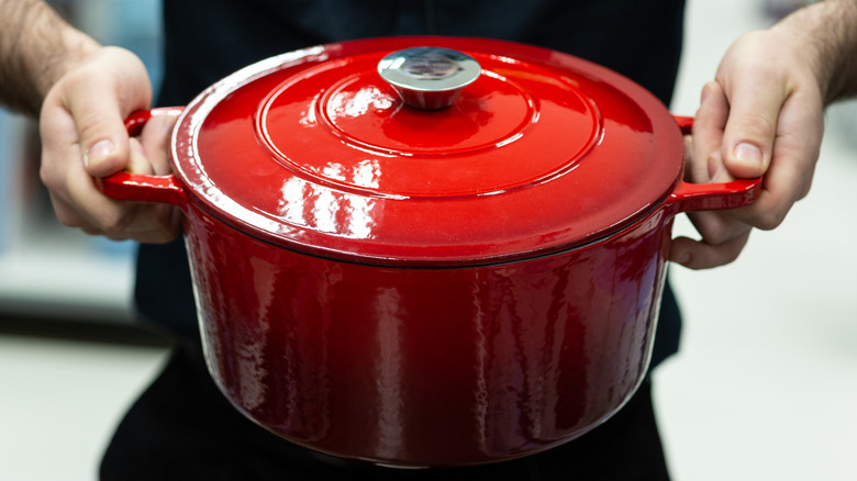 A close-up of someone holding a red Dutch oven