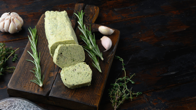 a log of compound butter with herbs and garlic on a wooden board