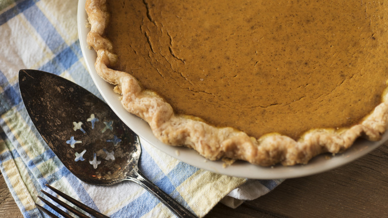A homemade pumpkin pie next to a pie server on a tablecloth