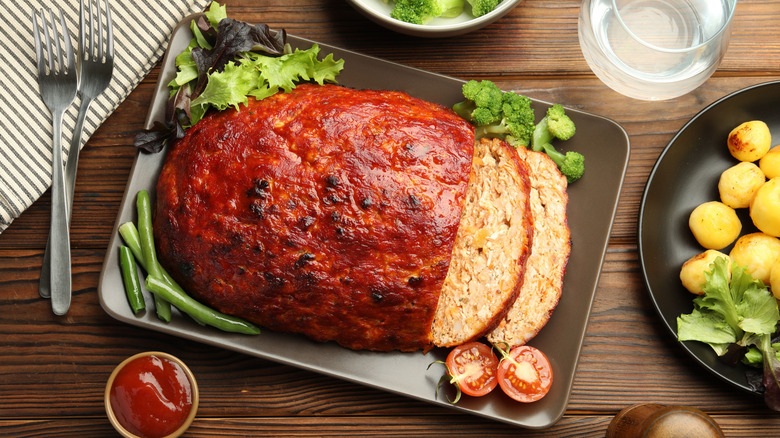 Turkey meatloaf sliced on a black plate with vegetables