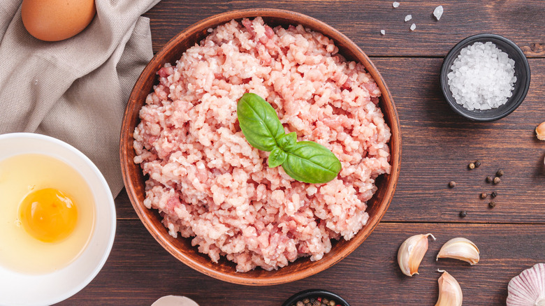 Ground raw turkey in a bowl surrounded by egg, salt, and garlic