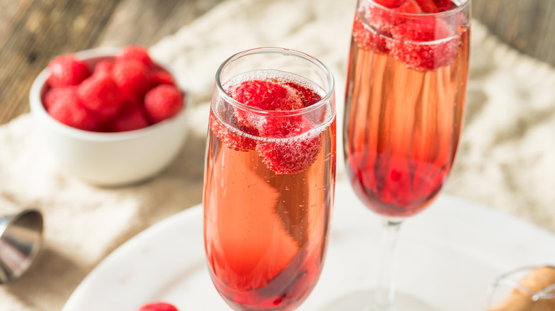 Two red colored champagne drinks with raspberries