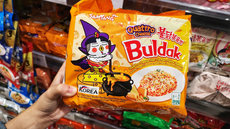 Someone holding a package of Buldak Quattro Cheese spicy ramen in a supermarket aisle