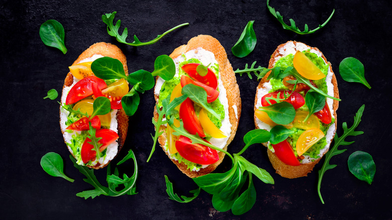 Crostini topped with whipped feta, pesto, tomatoes, and herbs