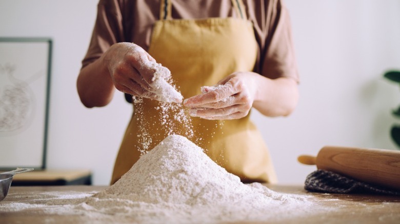 A baker sifts a mound of flour on a kitchen counter with her fingers