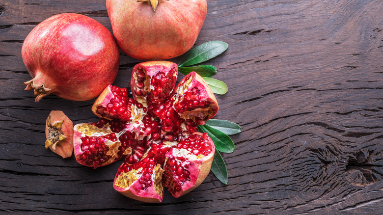 A pomegranate cut into sections with a whole pomegranate nearby.