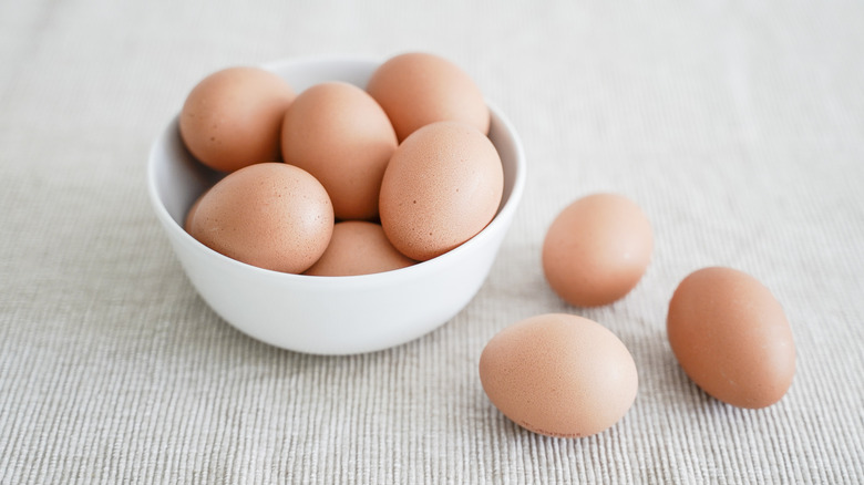 Whole brown eggs in a bowl with three eggs on side on a linen colored material