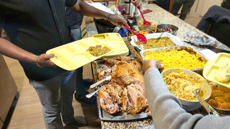 People serve themselves food from a Thanksgiving buffet at home