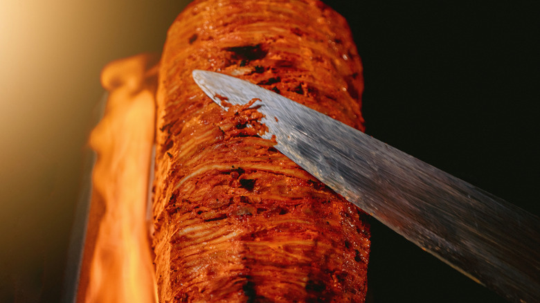 Cooked al pastor on a spit being sliced with a knife