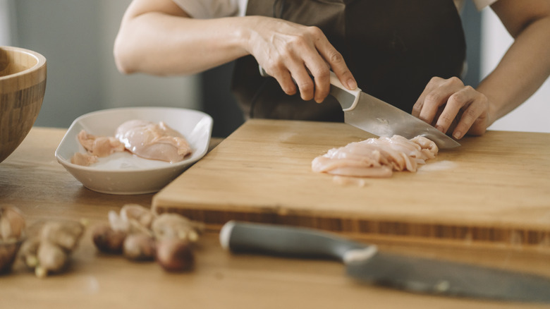 person slicing raw chicken