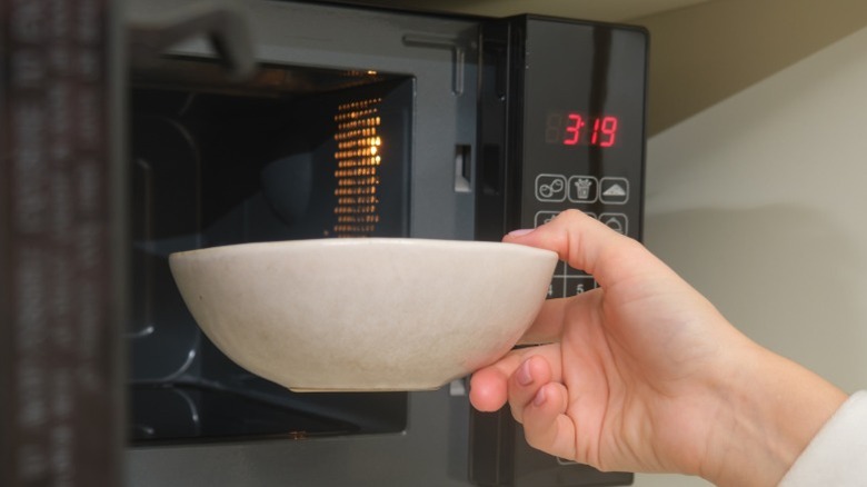 A hand holding a bowl in front of an open microwave.