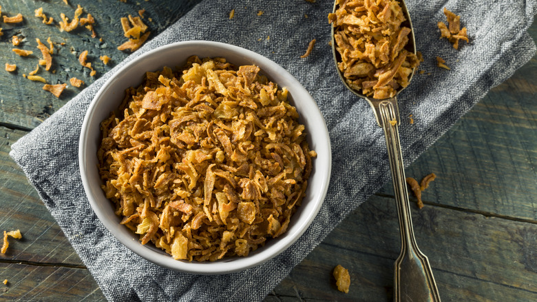 Crispy fried onion slices in bowl with a spoon on a kitchen towel