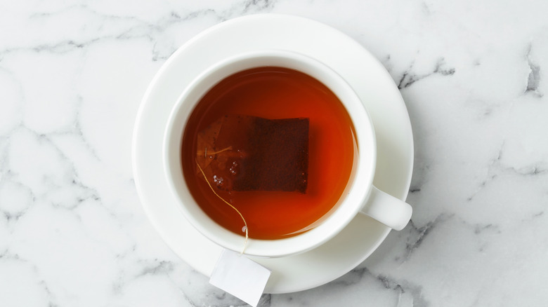 Top view of white tea cup and saucer with black tea and tea bag