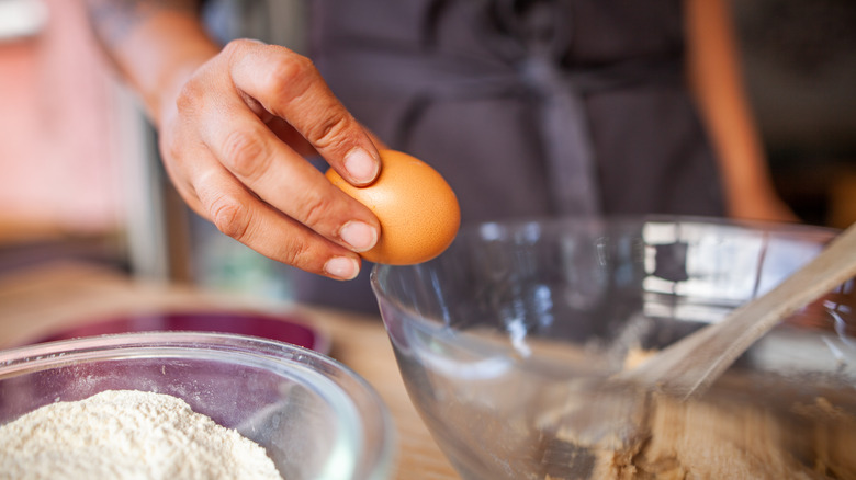 A baker cracking an egg directly into bowl of ingredients