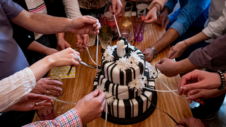 People preparing to do a wedding pull around a black and white iced wedding cake