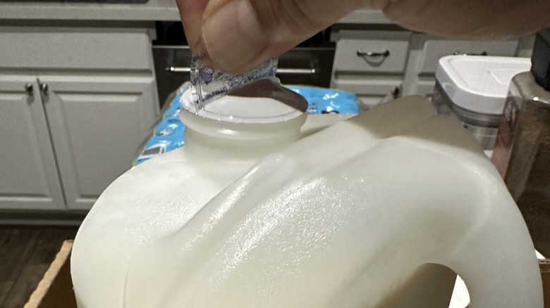A person's hand peels off the tab on a plastic milk jug