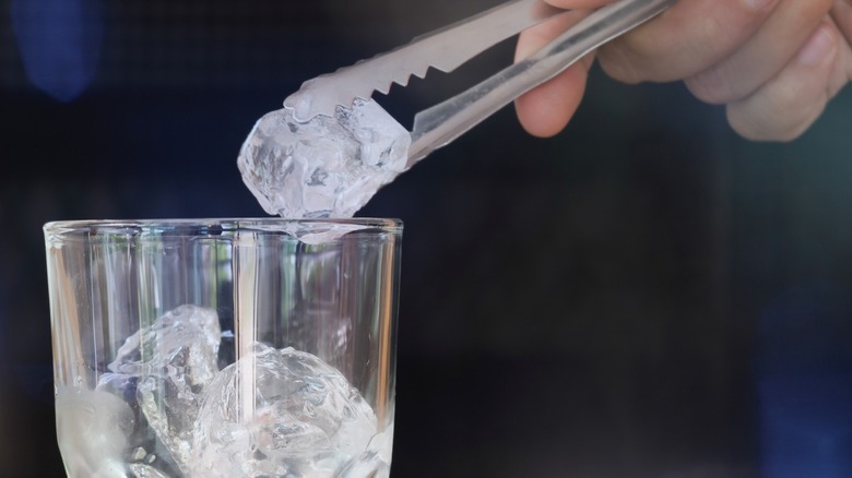 A person puts ice into a glass with metal tongs
