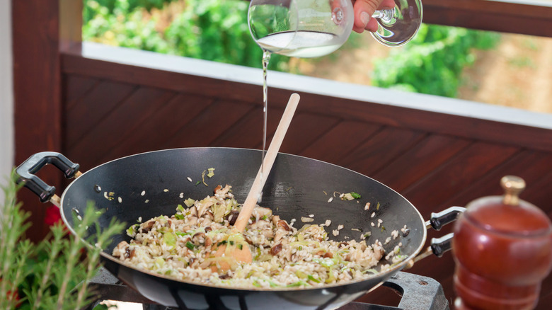 pouring white wine from a glass into a skillet with risotto cooking