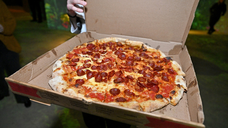 A New York Style pepperoni pizza in a pizza box being held by someone.