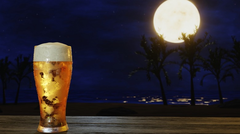 A glass of beer before a night sky and a full moon.