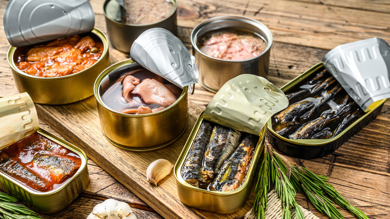 Different types of canned seafood on a wooden board