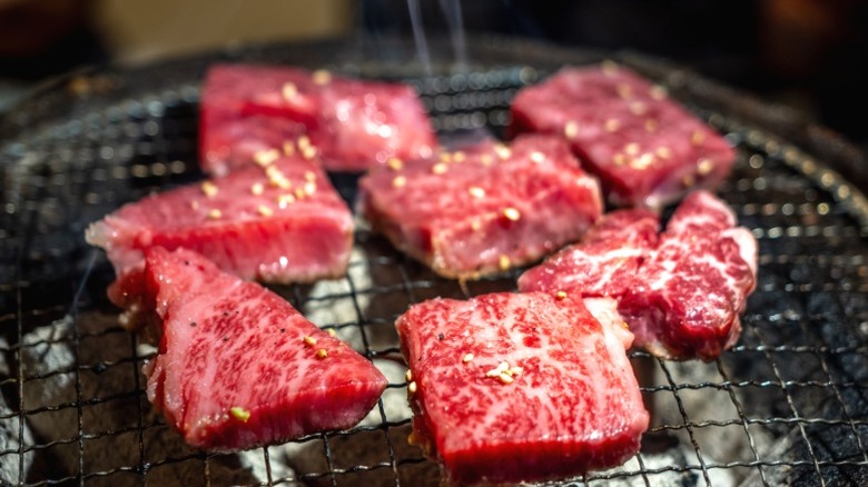 Cubes of Kobe beef cooking on a grill rack.