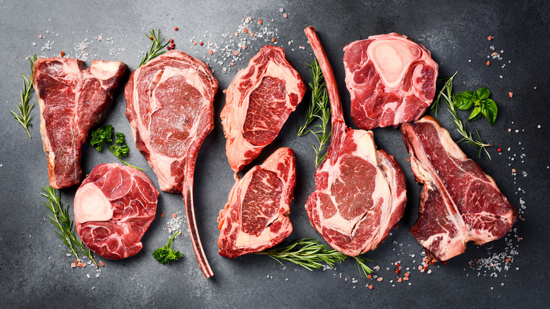 An array of raw beef steaks with herbs and salt