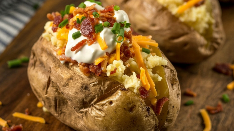 A loaded baked potato with cheese, sour cream, bacon, and green onions on it