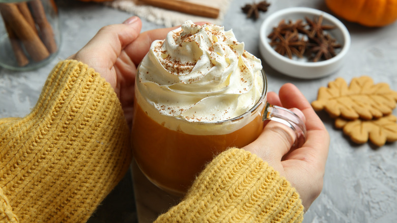 Woman in sweater cradles pumpkin spice latte with cream