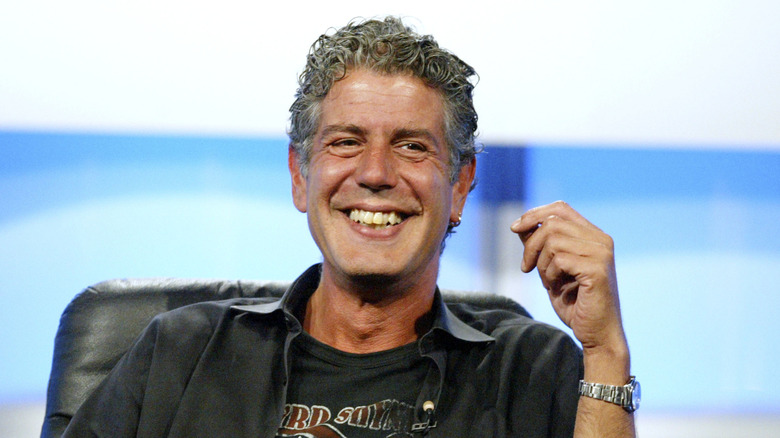 Anthony Bourdain sitting in black leather chair and smiling