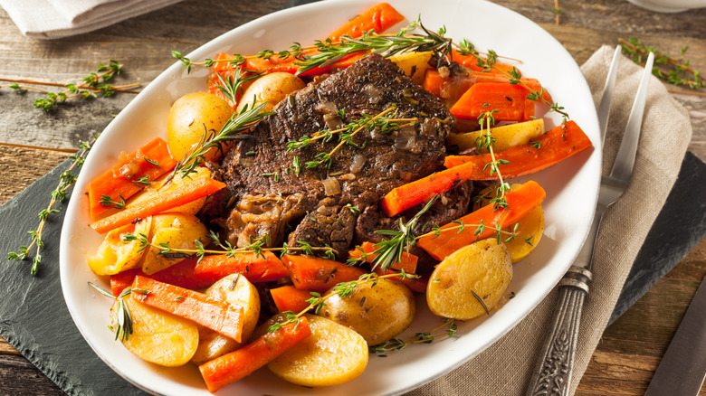 Platter with beef pot roast, carrots, potatoes, and sprigs of thyme and rosemary